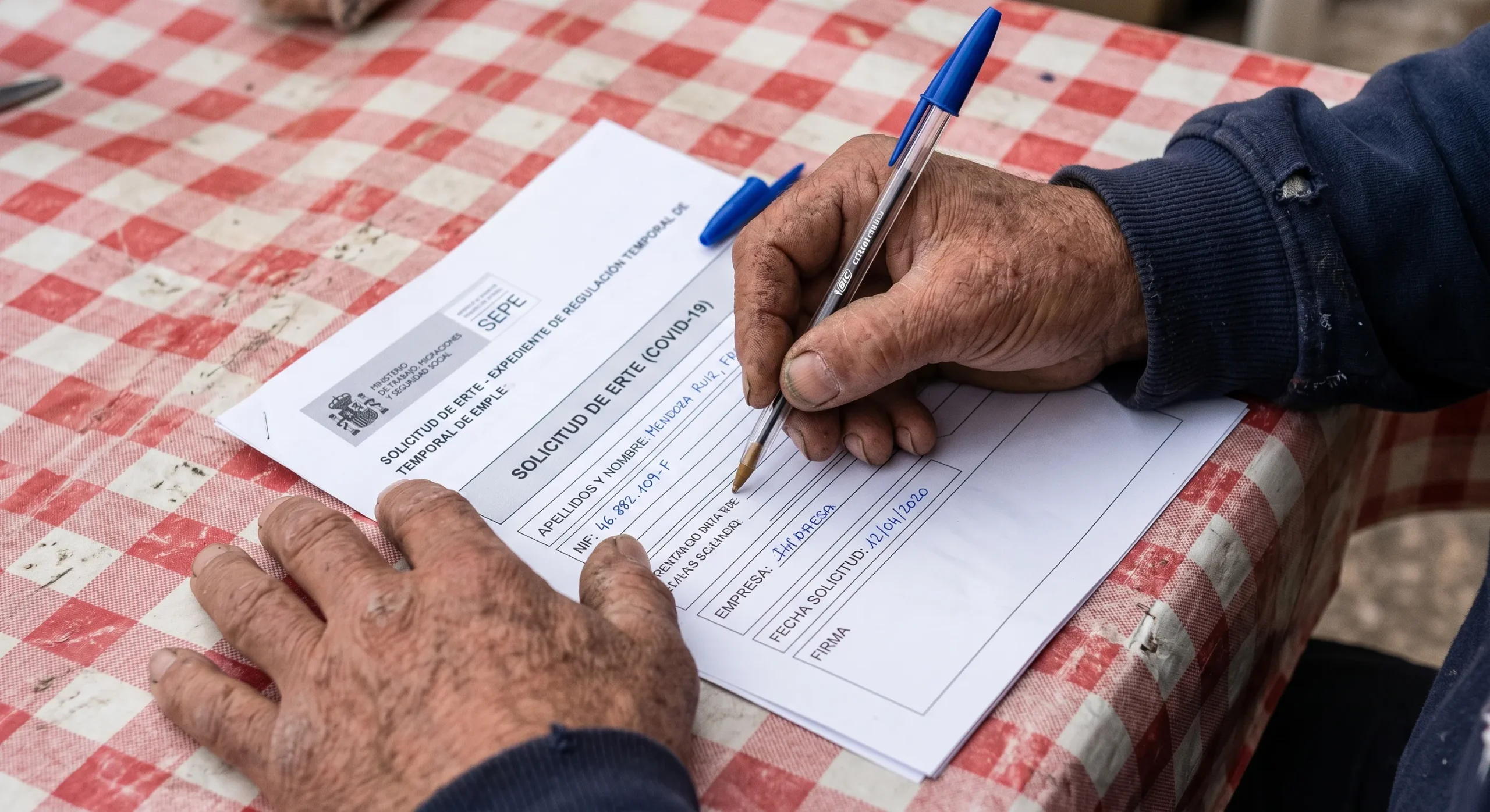 Manos de trabajador con síndrome del túnel carpiano rellenando documentos de incapacidad permanente en la mesa
